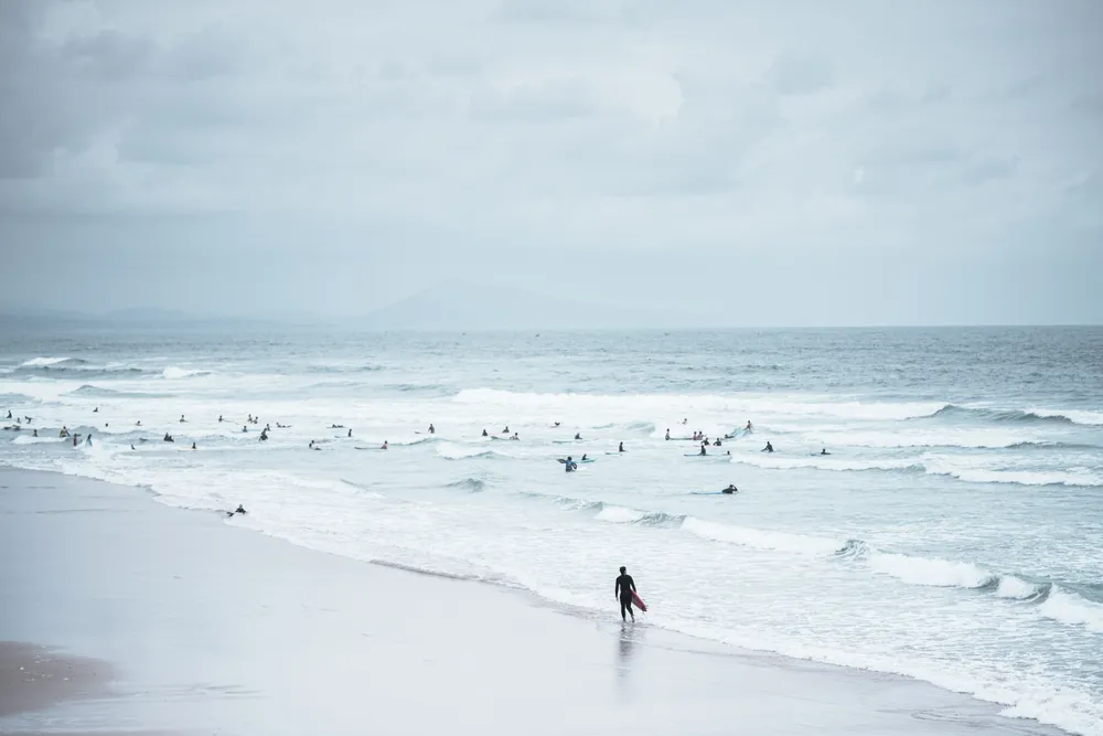 "A morning in Biarritz, France, where surfing has become a ritual. 
As often along the Basque coast, Spanish hills appear faintly in the distance. 
Surfers are everywhere. 
One stands apart, moving towards the waves. 
A brief pause, a moment of alignment with the ocean."