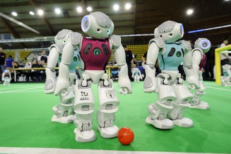 Nao robots race—slowly—to the open ball. 