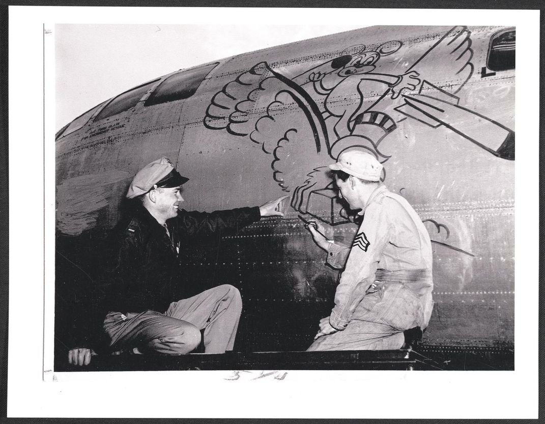 one airman painting a plane while other points