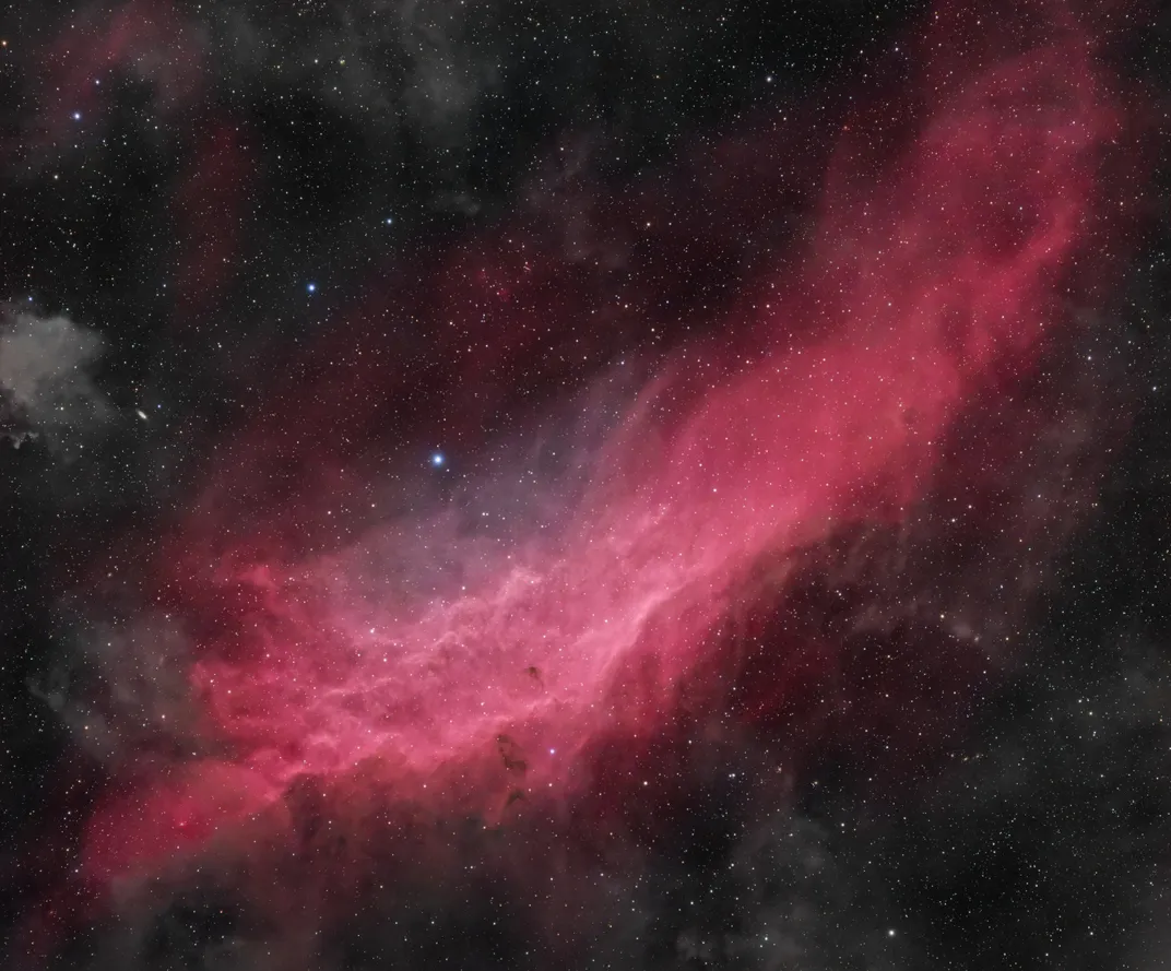 A reddish-pink emission nebula in the vague shape of the state of California