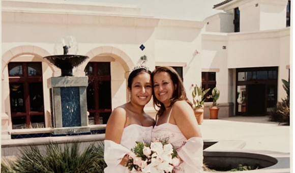 Quinceañera (fifteen-year-old girl) wearing a long strapless dress and posing by her mother's side.