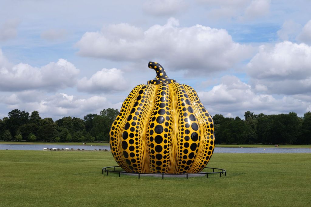 Large yellow pumpkin covered in black polka dots on a grassy area surrounded by trees