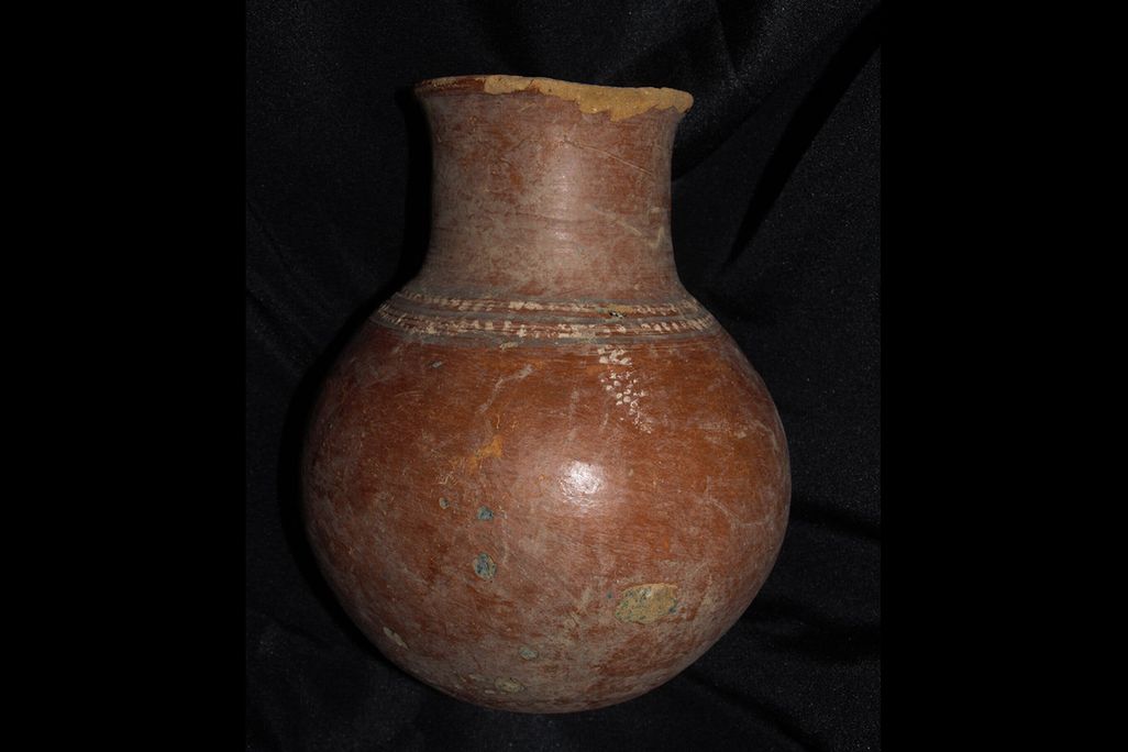 A reddish high-necked pot with some painting and visible cracks; mostly reddish-brown with specks of green and blue