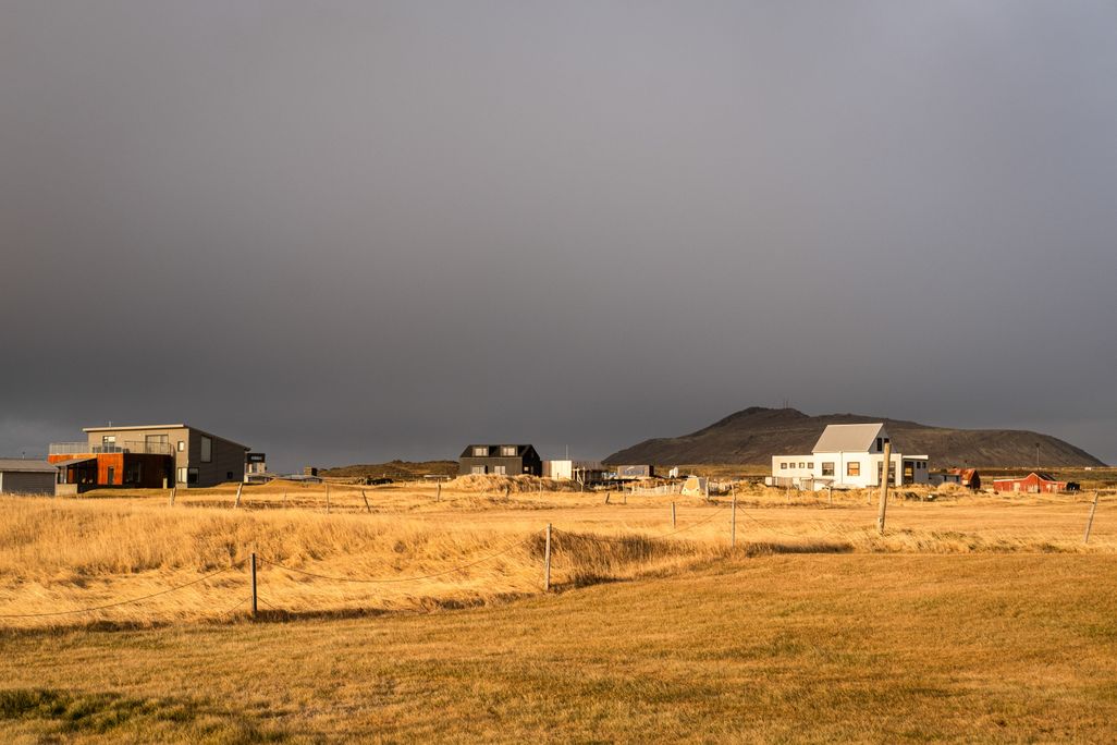 A couple of buildings at the back of a field with a dark sky overhead
