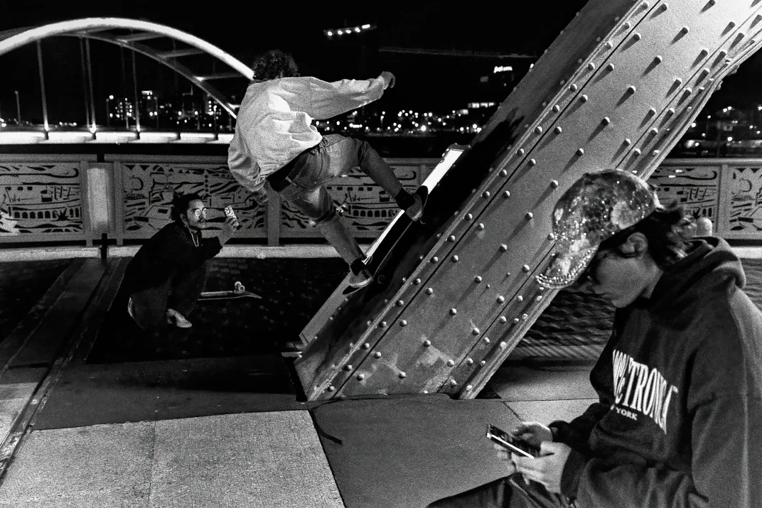 Black and white photo of kids skateboarding on bridge