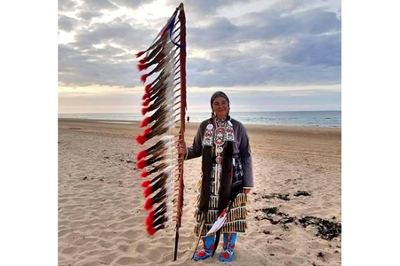 Command Sergeant Major Julia Kelly (U.S. Army retired), one of 80 Native American delegates to the 75th anniversary observance of D-Day, stands on Omaha Beach. Kelly holds an eagle feather staff, an American Indian symbol of respect, honor, and patriotism. (Courtesy of Julia Kelly)