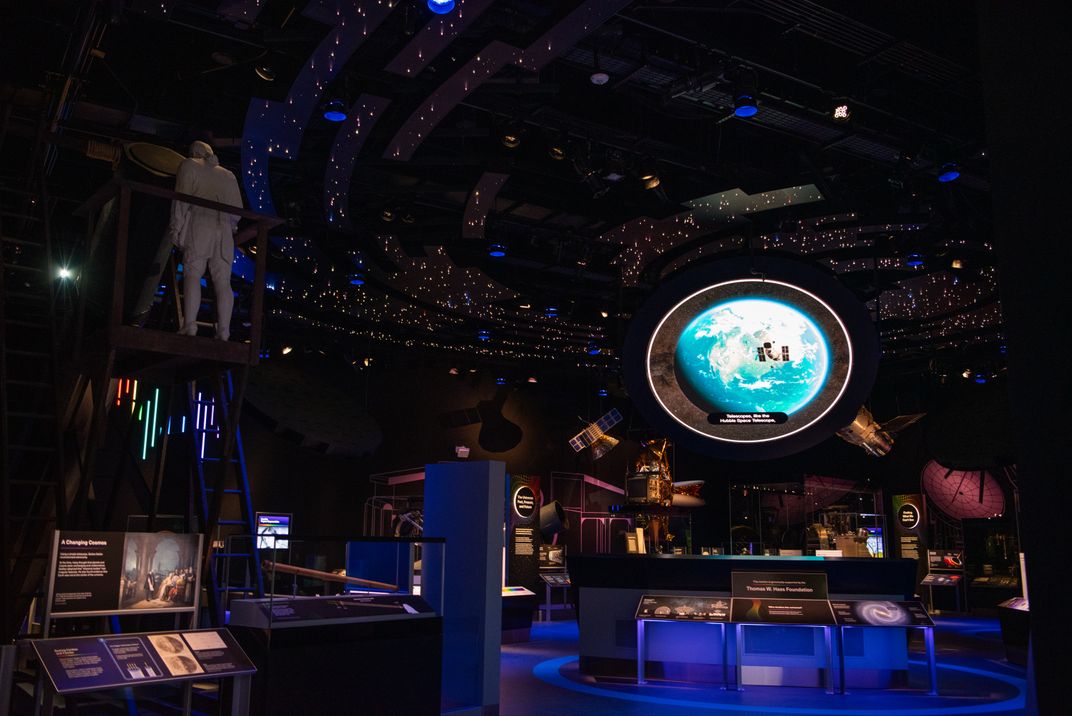 a museum gallery that is dark with displays and a circular screen with Earth in the center