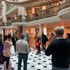 People stand and listen to a speaker in a brightly lit museum room underneath a large gold art installation.
