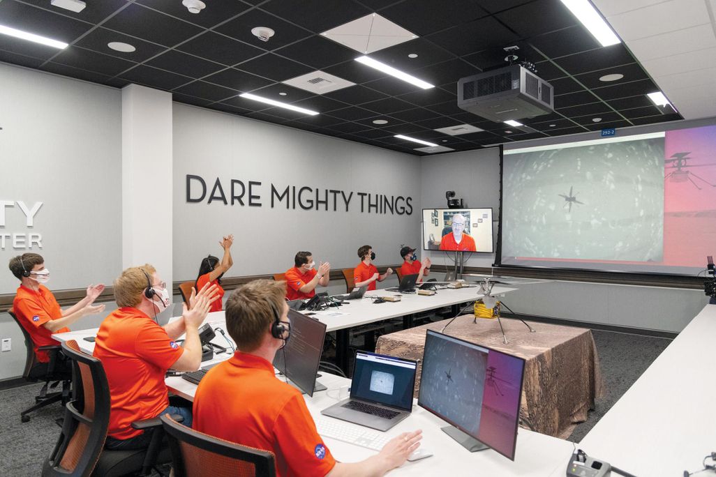 team of people in orange shirts sitting and clapping while looking at a screen