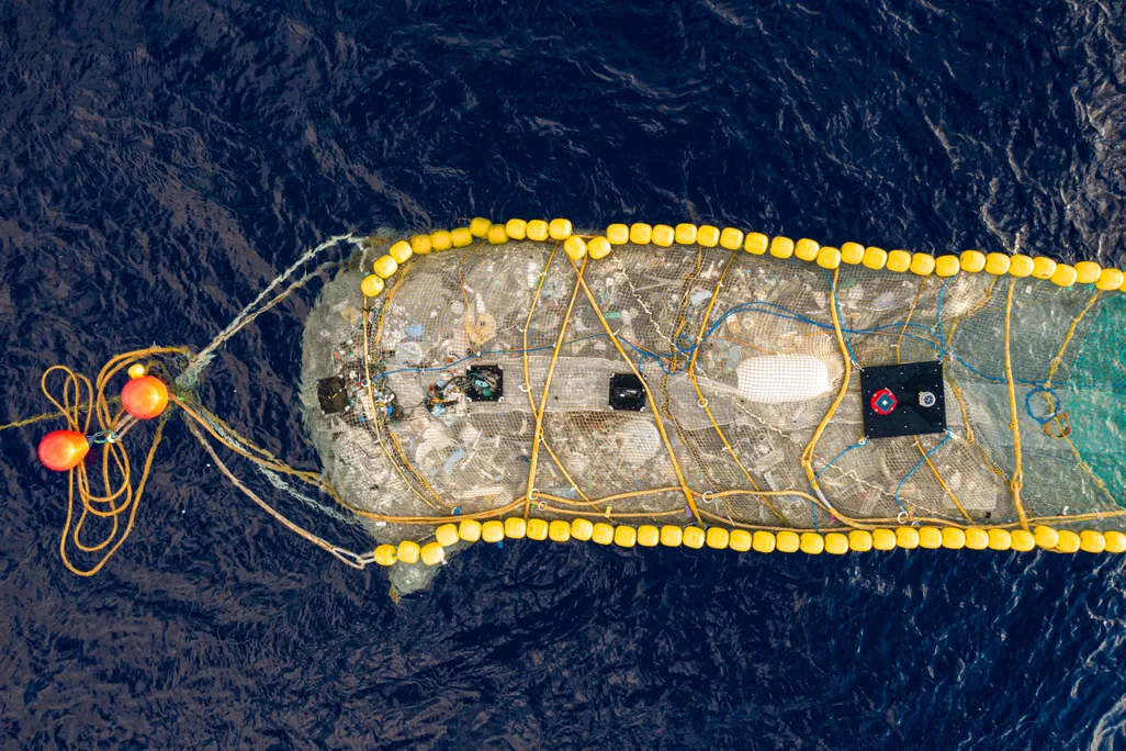 Ariel photo of trash collection device resembling floating pool lane lines with a large net filled with plastic trash