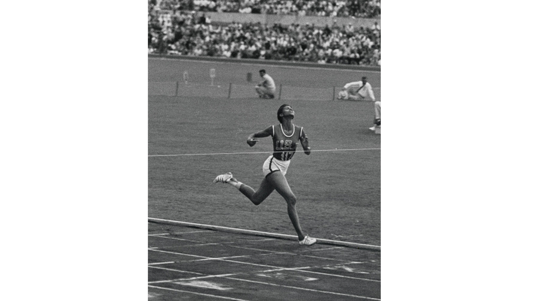 Black and white photo of a woman running towards the finish line on a track