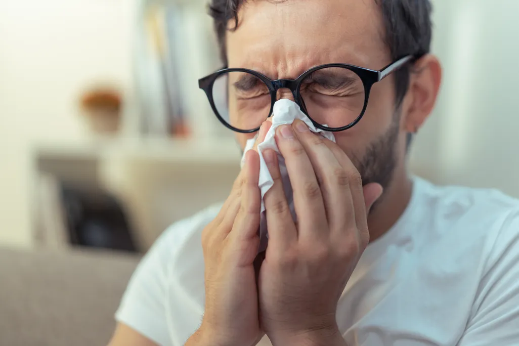 man with glasses blows his nose