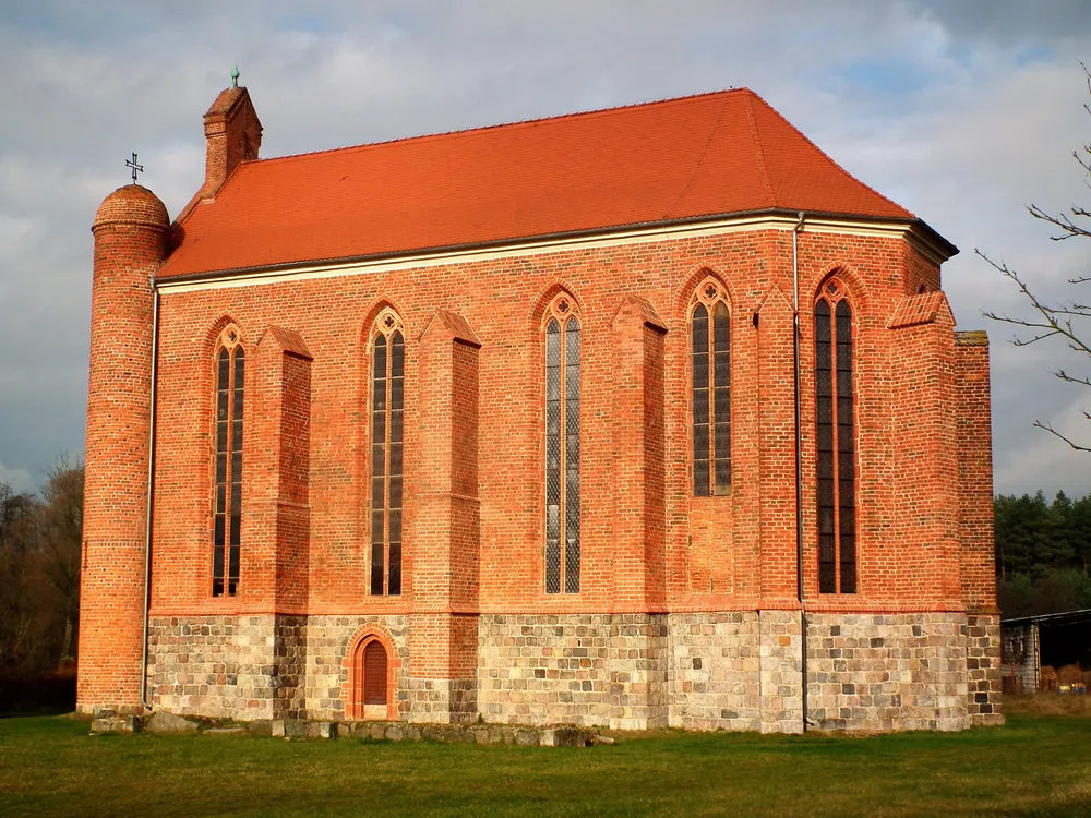 The exterior of an orange brick chapel with skinny, tall Gothic windows, a gabled red roof and a curved nave on one end.
