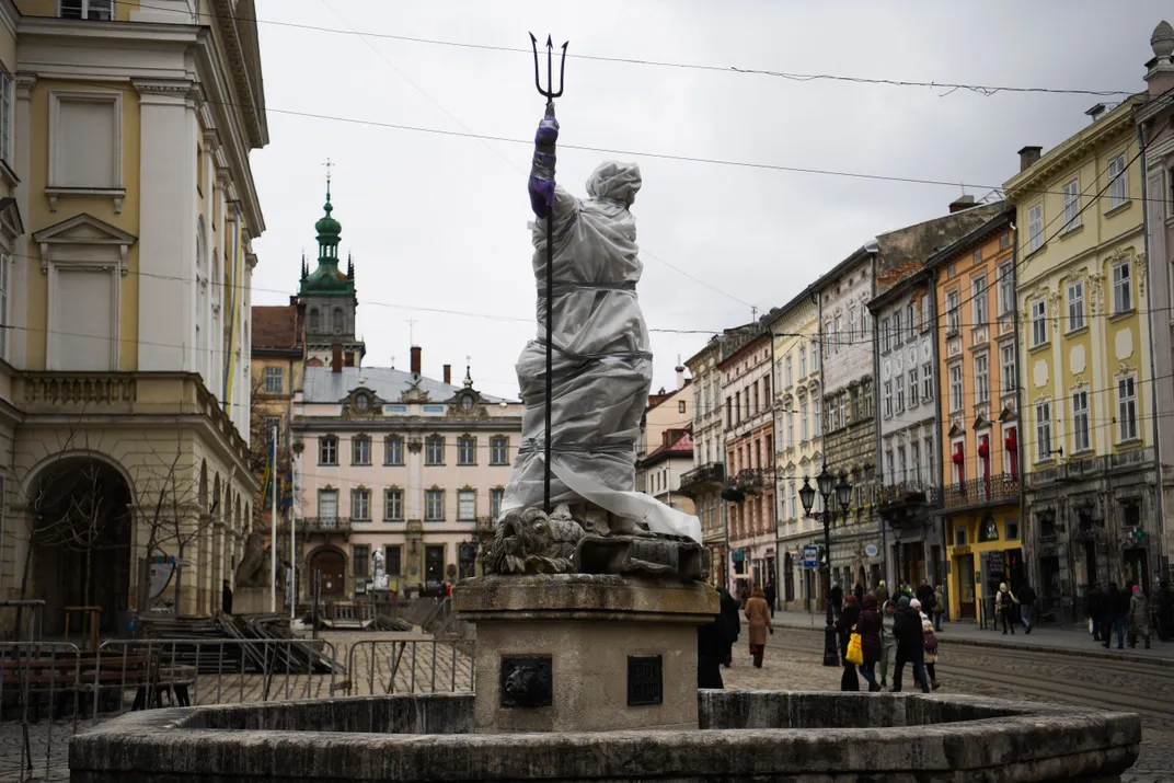 Pedestrians walk past a wrapped statue next to the Latin Cathedral in Lviv on March 5, 2022.