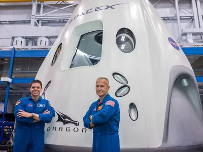 Commercial crew astronauts Bob Behnken (left) and Doug Hurley (right) stand in front of a SpaceX Dragon mock-up at the Johnson Space Center. 