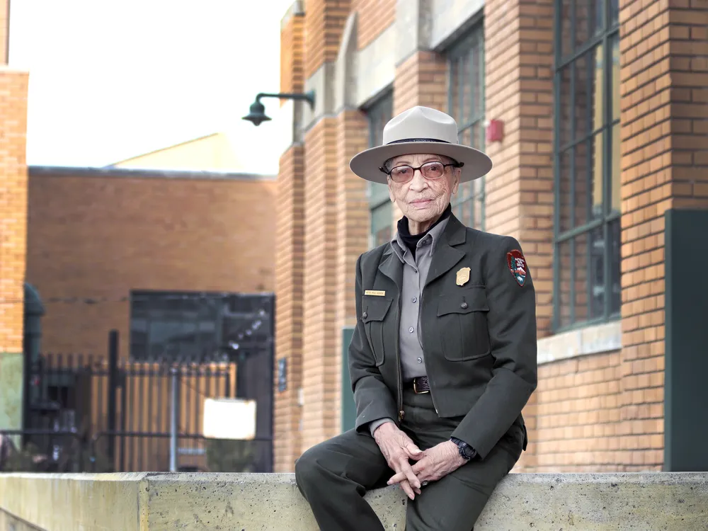 Betty Reid Soskin, an elderly Black woman in a green-gray NPS ranger uniform with a wide-brimmed hat
