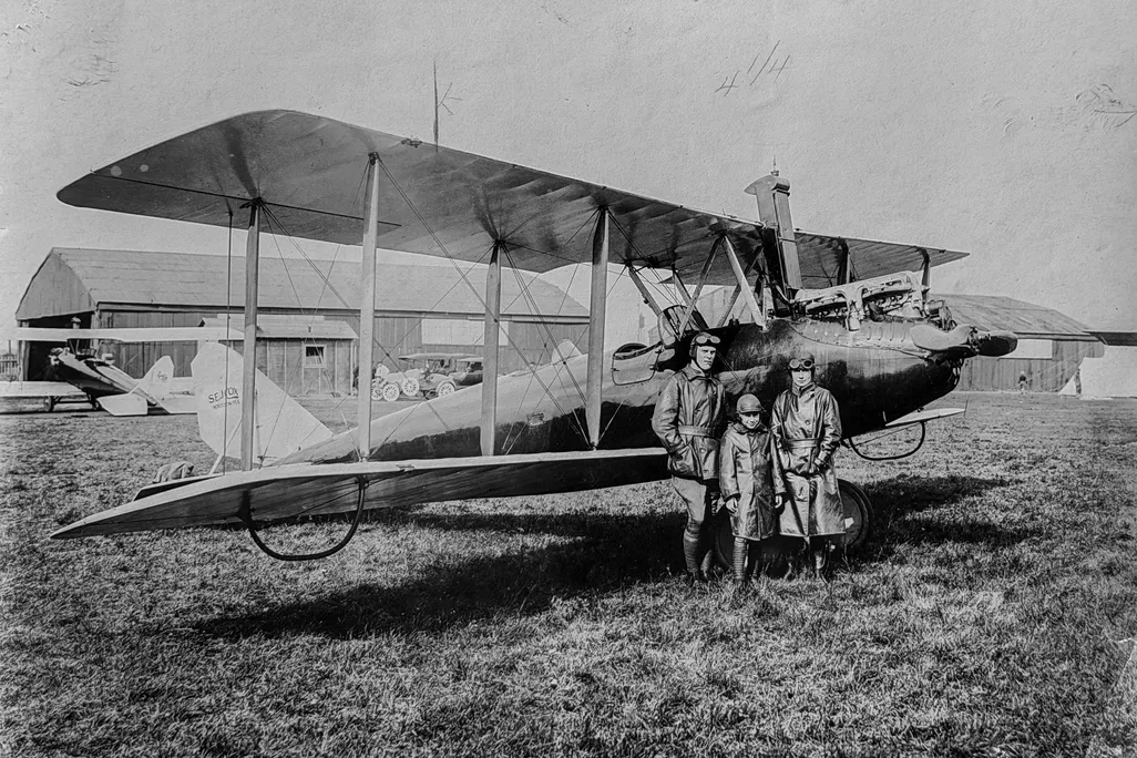 A black and white photo showing a small airplane with three people standing next to it in a field