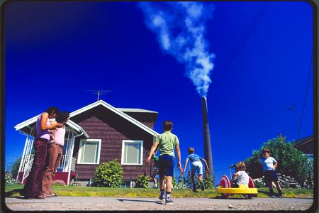 “Children play in yard of Ruston home, while Tacoma smelter stack showers area with arsenic and lead residue.” Gene Daniels, Ruston, Washington, August 1972.