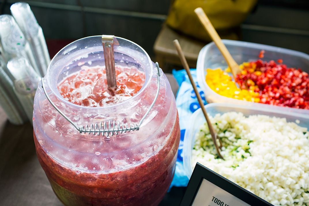 A container of fresh, red agua fresca is mixed on a table.