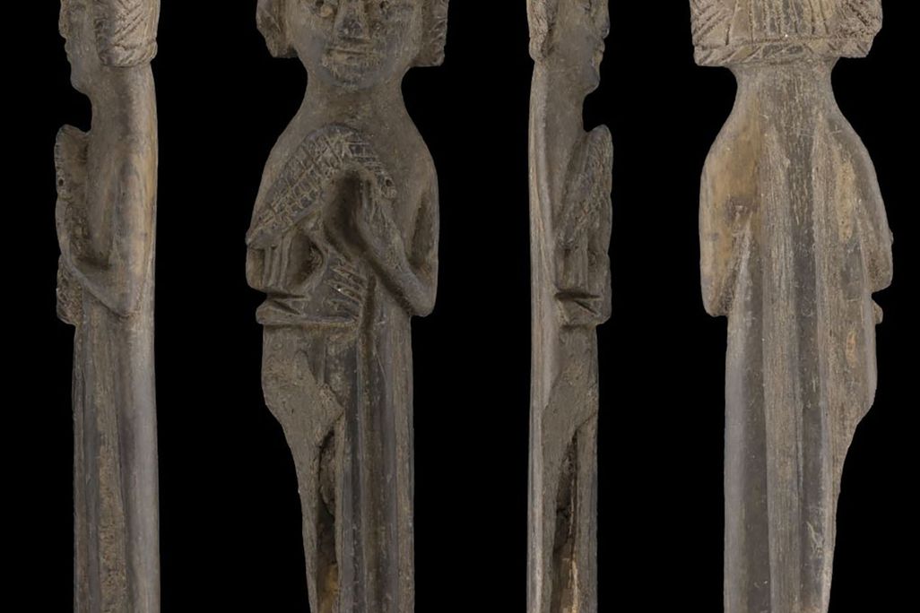 carved wooden figure of person with crown and falcon on right arm