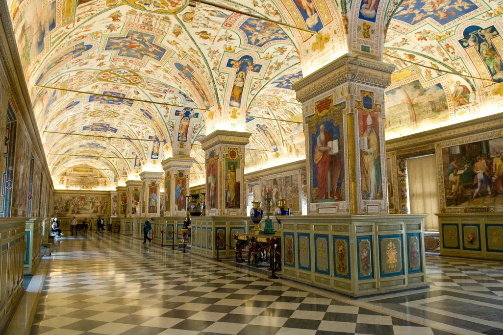 An ornately decorated hall with black and white checkered floors and depictions of saints covering the arched ceilings