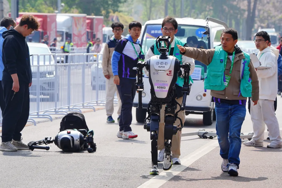 A humanoid robot takes a fall while another races past