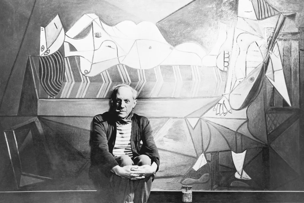 Black and white image of Pablo Picasso posing in front of one of his paintings