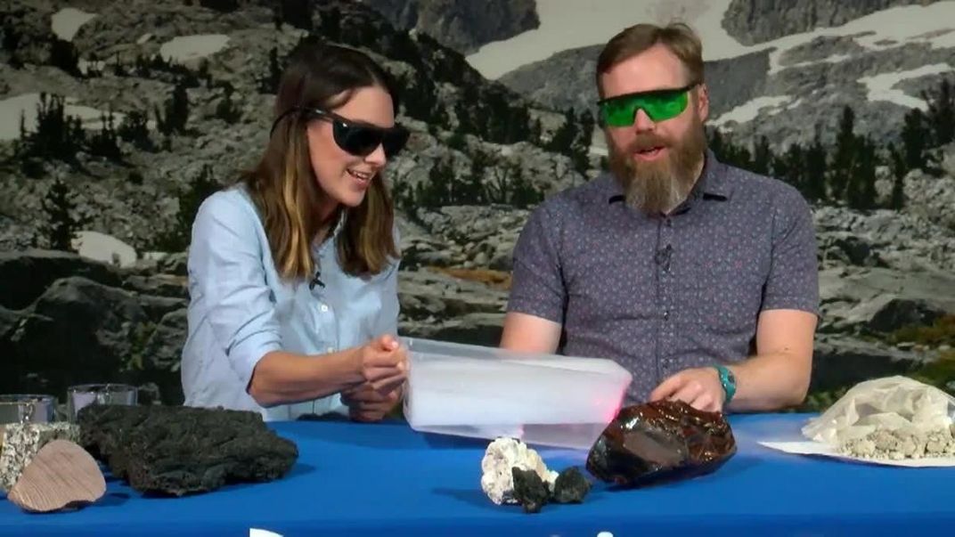 Two people sitting at a table with rock samples on it. 