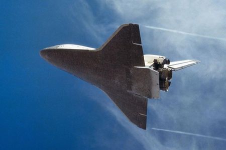 Underside view of space shuttle in flight with blue sky background.