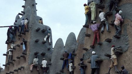 Masons climb up the sides of the Great Mosque to replaster the surface with mud.