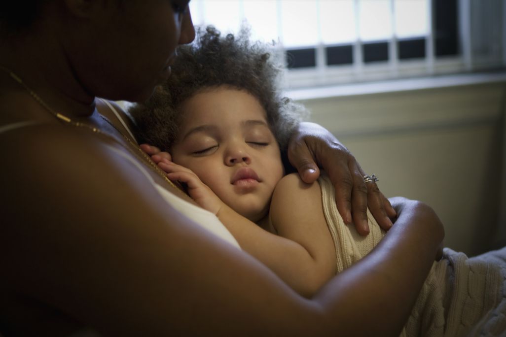 A sitting mother holds a sleeping child to her chest