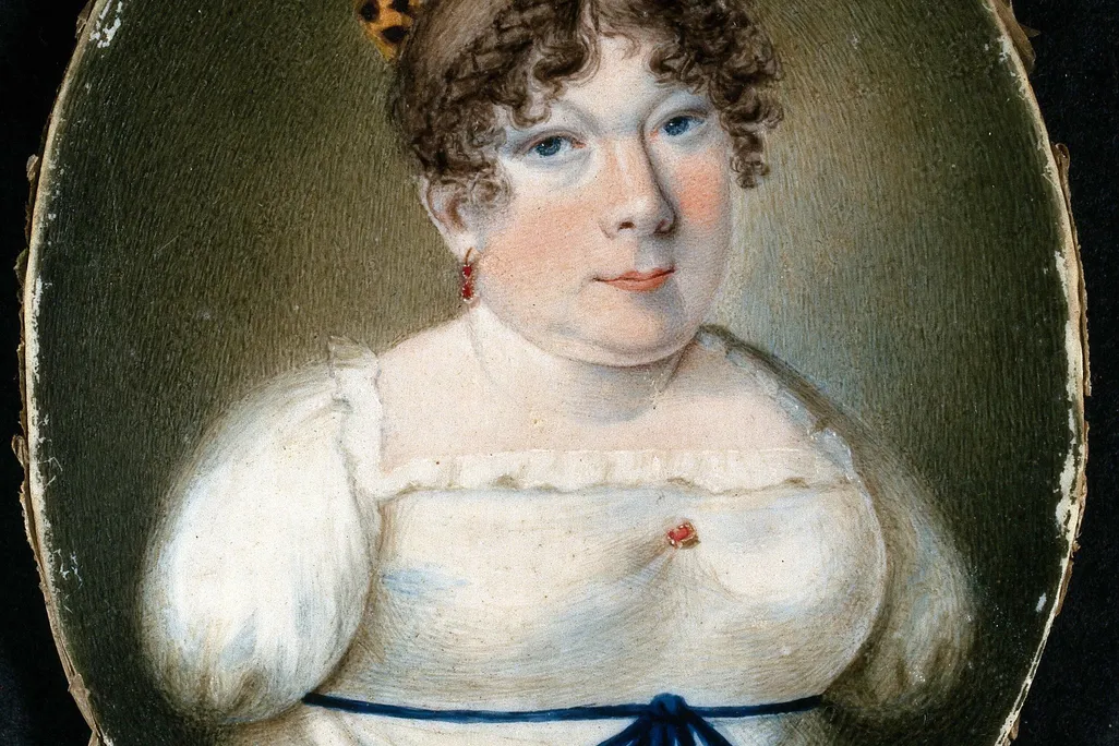 A miniature portrait of a white woman with curled brown hair in a white empress dress with a blue ribbon; her arms end below the shoulder, where her dress is pinned