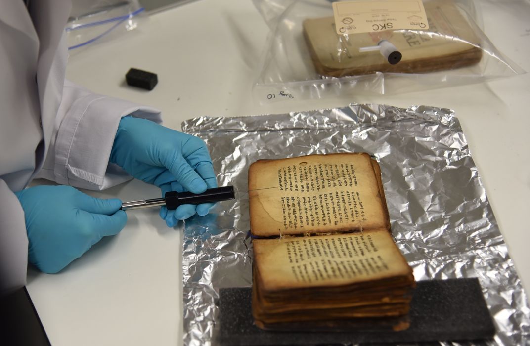 gloved hands take a syringe of air near an old book on top of tinfoil