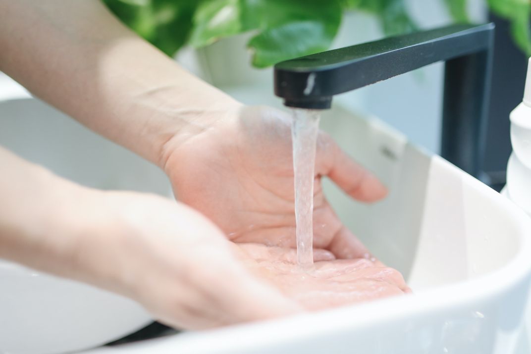 Person washing hands in sink under running faucet