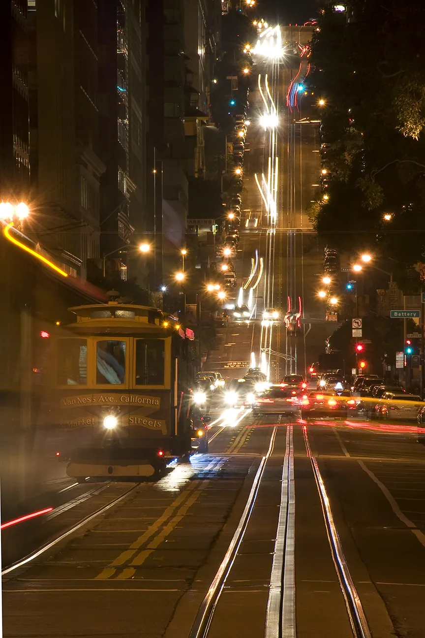 A train car goes down a busy San Francisco street at night