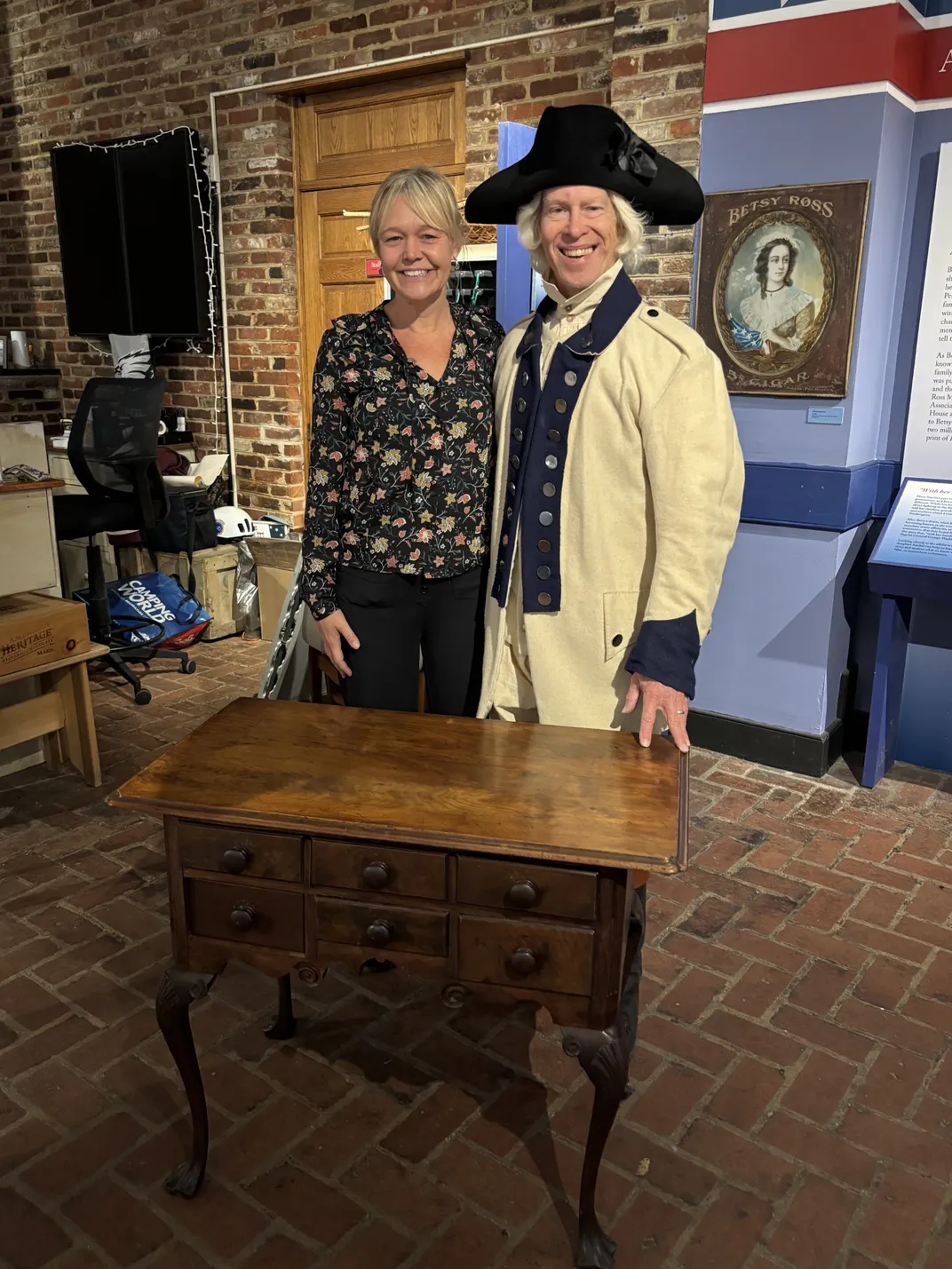 A woman standing next to a man in a colonial costume next to a desk