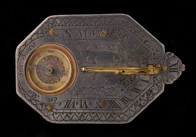 A richly decorated pocket sundial, seen from above. Its compass is surrounded by engraved notations describing eight directions in both French and English. A signature, Bourgaud Nantes, sits at the center of the sundial.