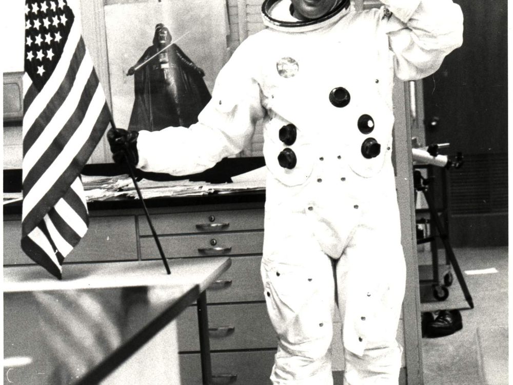 Informal classroom portrait of teacher Herbert Stephen Desind (1945-1992), wearing a reproduction Apollo-era spacesuit, holding an American flag; circa 1980s. Desind was a space flight aficionado, and his collection of photographs of aircraft and spacecraft was donated to the National Air and Space Museum in 1997. This image is part of the Herbert Stephen Desind Collection.