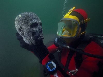 A diver holds a granite head, meant to be the head of a priest, from the Ptolemaic period. The now-hollow eyes were probably inlaid when it was first made in ancient Egypt.