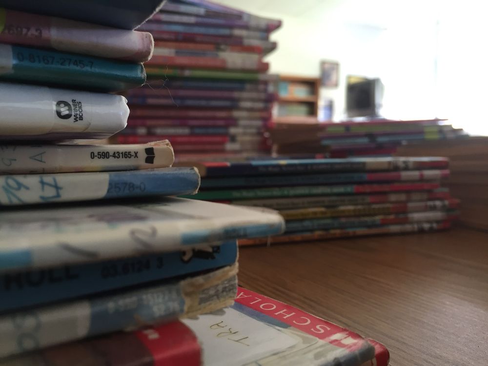 three small stacks of various books sitting on top of brown desk