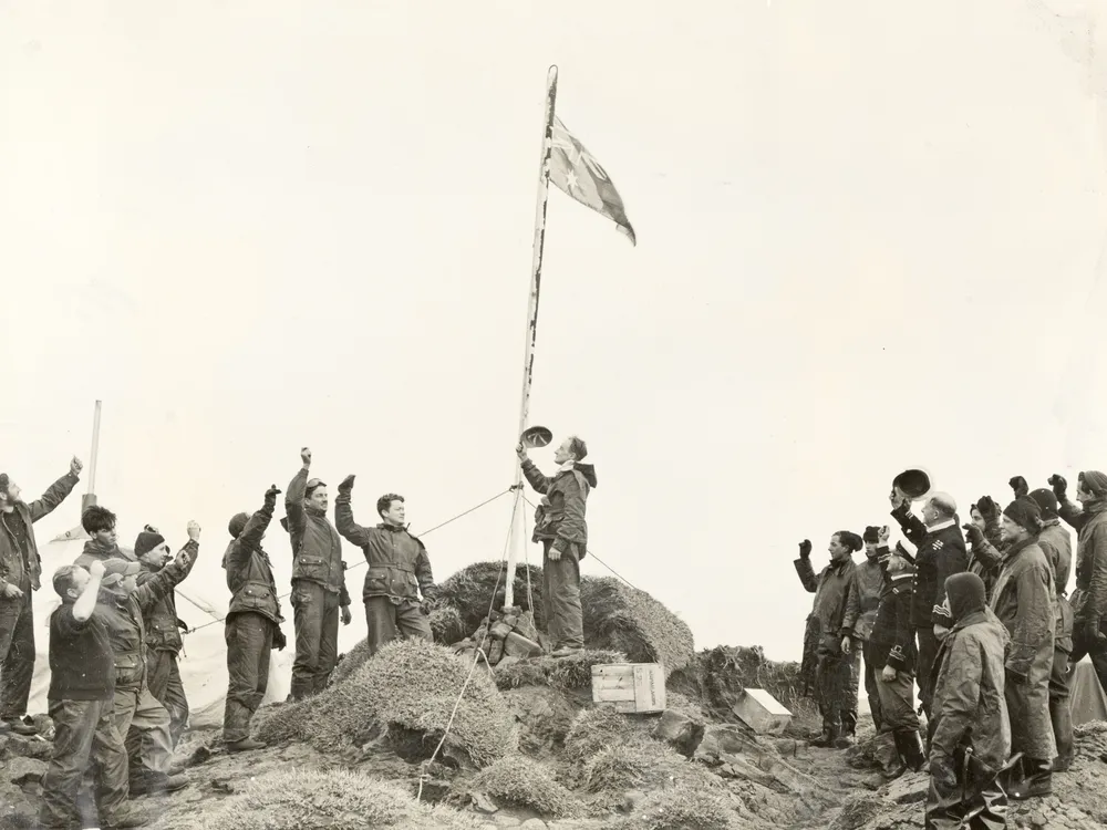 Black and white photo of men standing around a flag