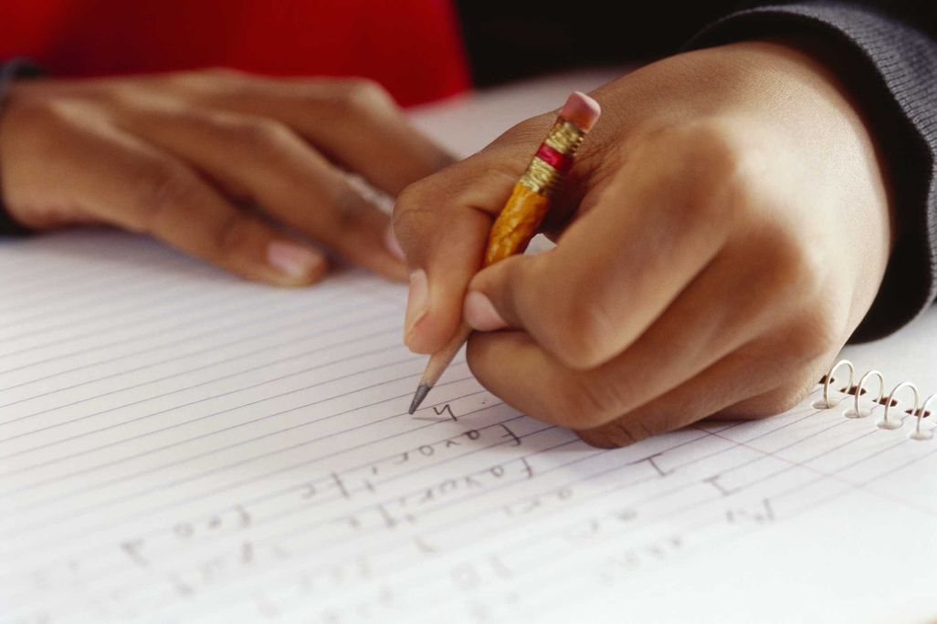 A child writes in a notebook using a pencil in their left hand
