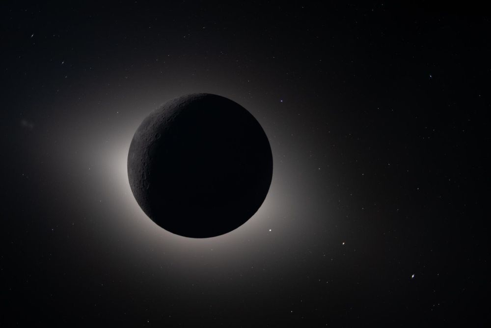 the moon appears as a dark circle with a faint white glow around it in a solar eclipse from space