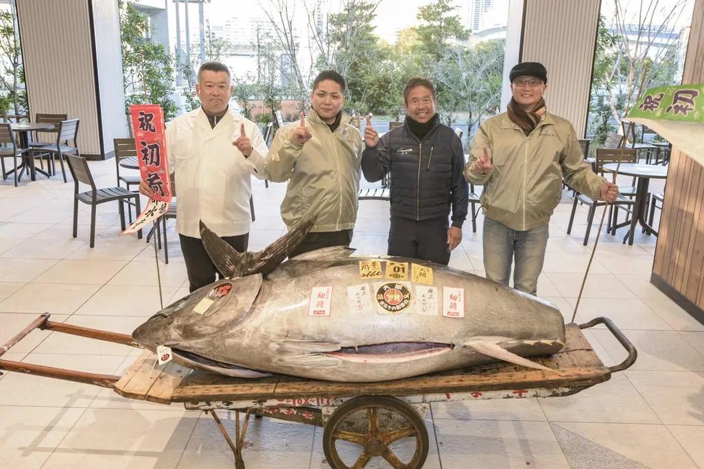 A giant fish on a rolling cart with four people standing behind it holding up their index finger in a No. 1 sign