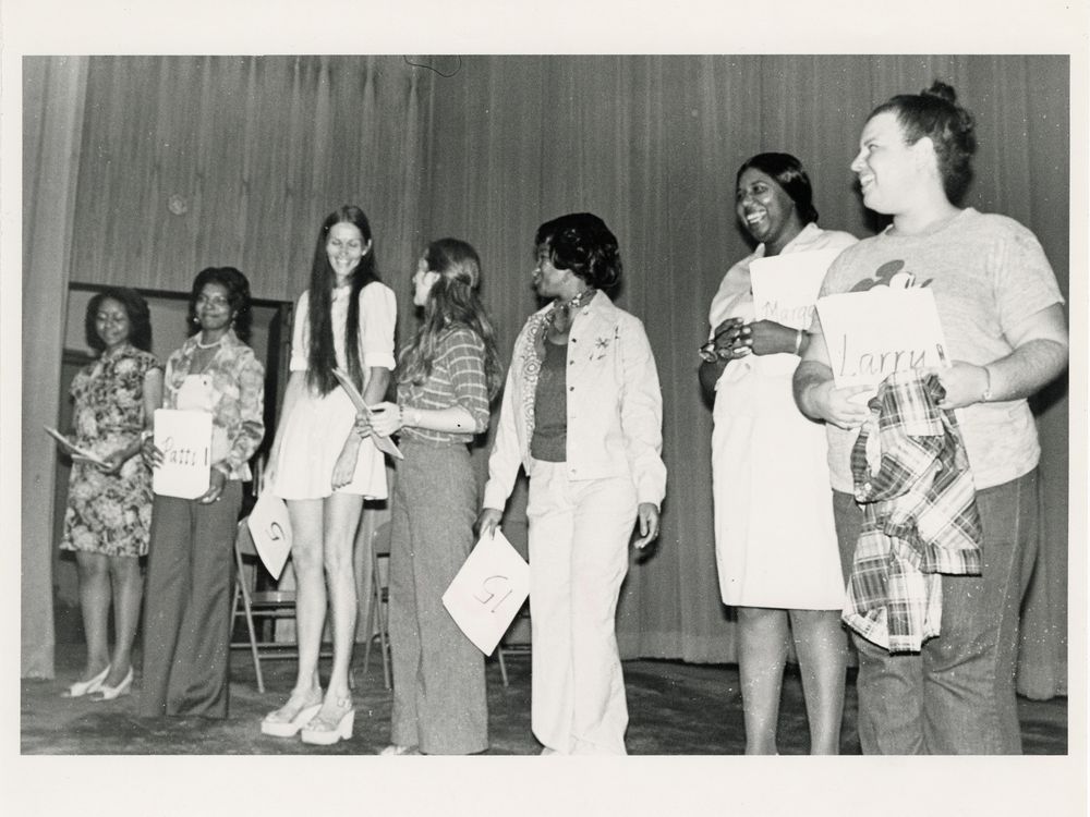 Candid photo of seven women holding papers standing in a line on stage.