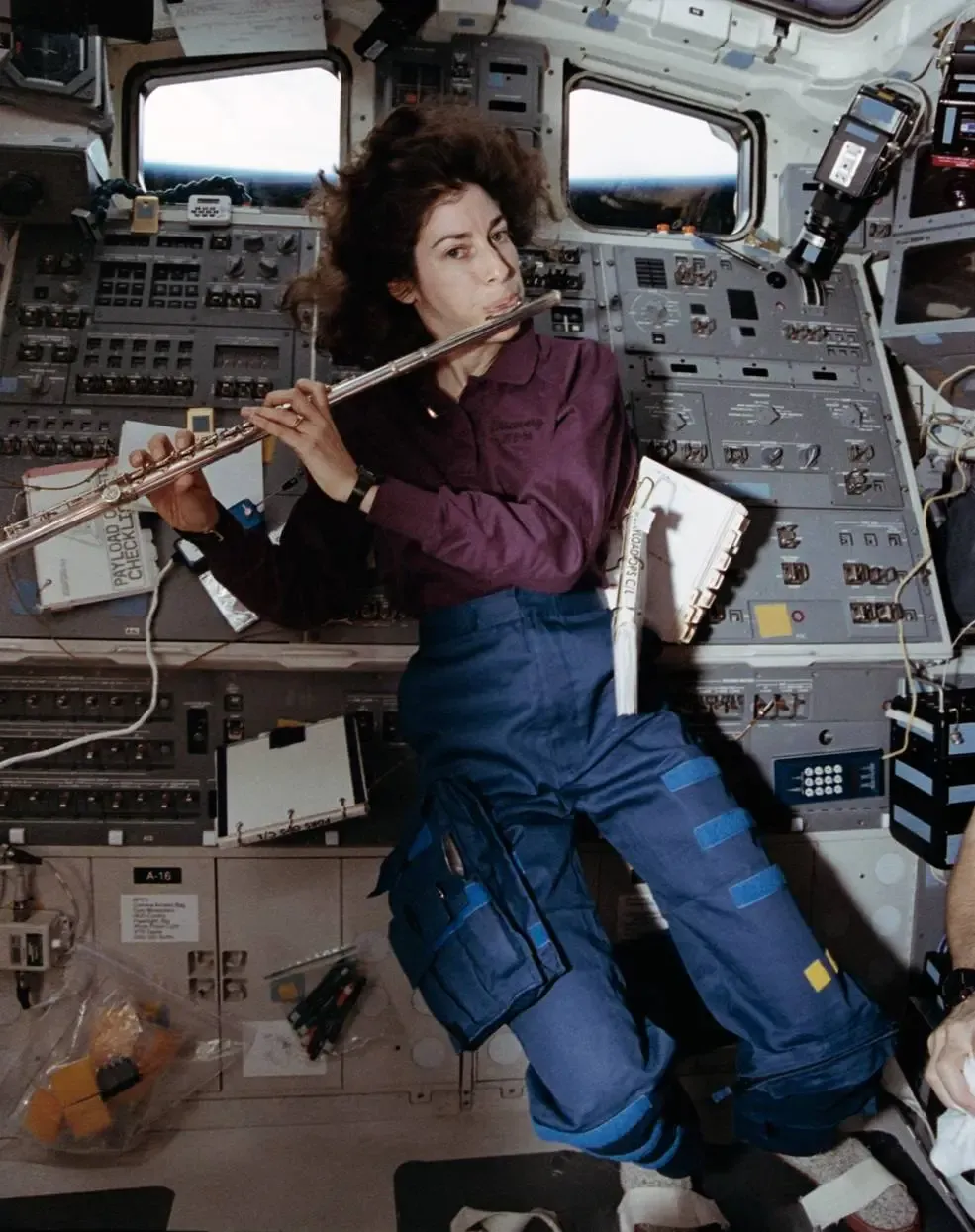 Ellen Ochoa plays her flute in front of a control panel in the ISS