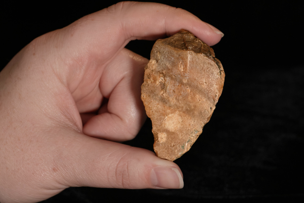 A hand holding a shaped stone tool against a black background