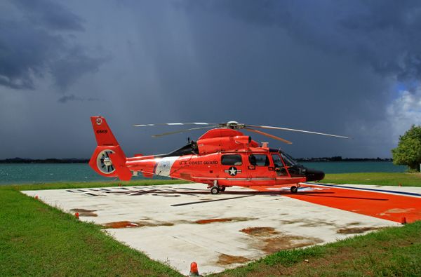 U.S. Coast Guard MH-65D Dolphin from Air Station Borinquen, on the helicopter pad at Sector San Juan, Puerto Rico, with an ever-present afternoon downpour in the background. thumbnail