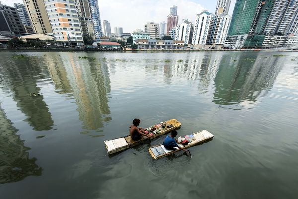 Two children riding a makeshift raft paddling on a river. thumbnail