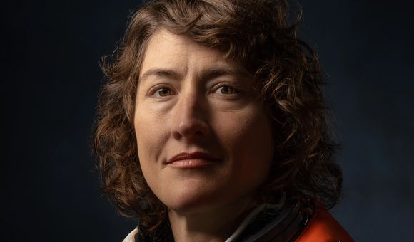 Dramatically-shot portrait of a white female astronaut in an orange spacesuit.